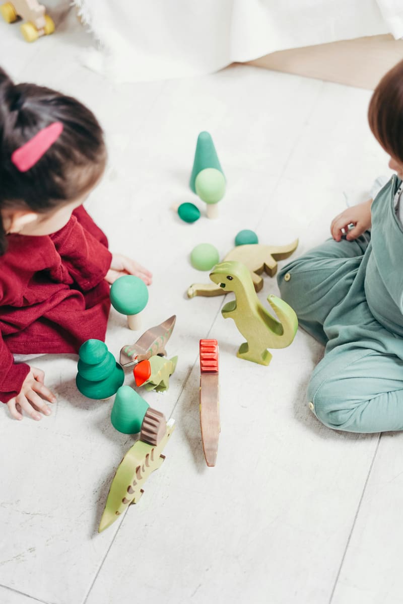 Zwei Kinder spielen mit Figuren und Holzspielzeug auf dem Boden