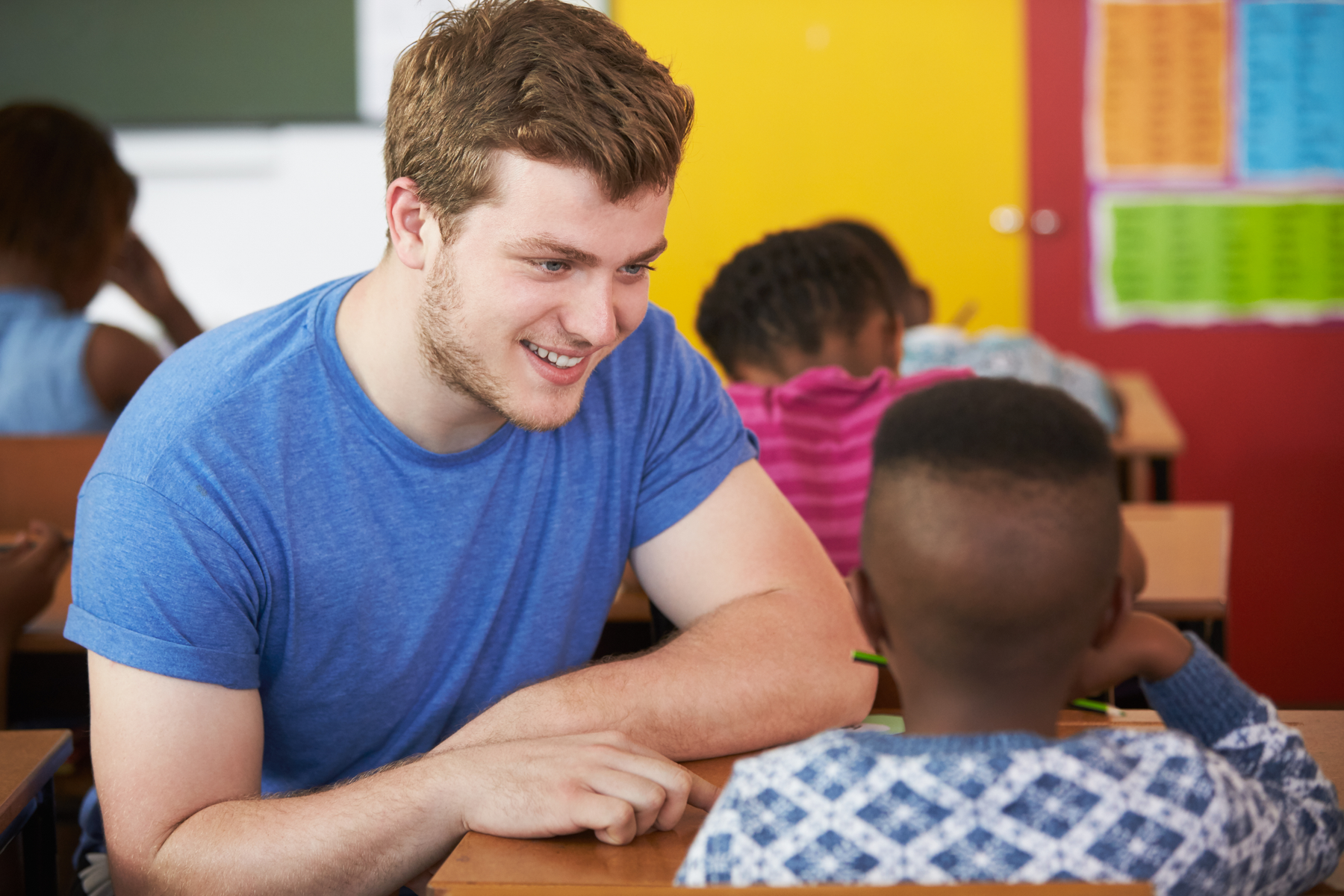 Ein junger Mann arbeitet konzentriert mit einem Kind in einem Klassenraum.